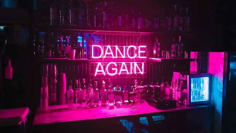 a neon sign with Dance Again mentioned on it and drinks surrounding it.