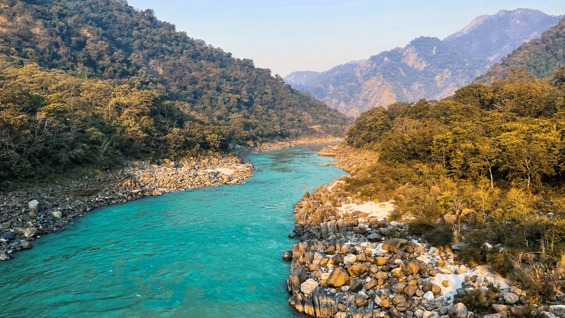Full view of the Ganges flowing between hills during daytime with a clear sky in the background.