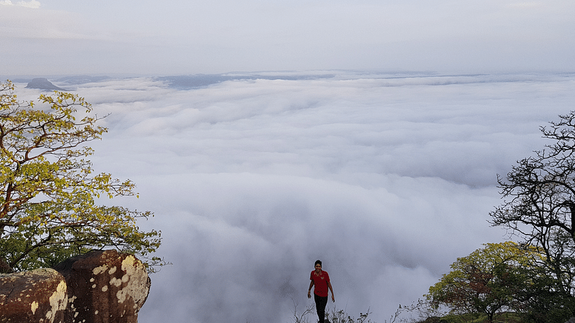a person posing for a picture on top of a mountain with clouds in the background