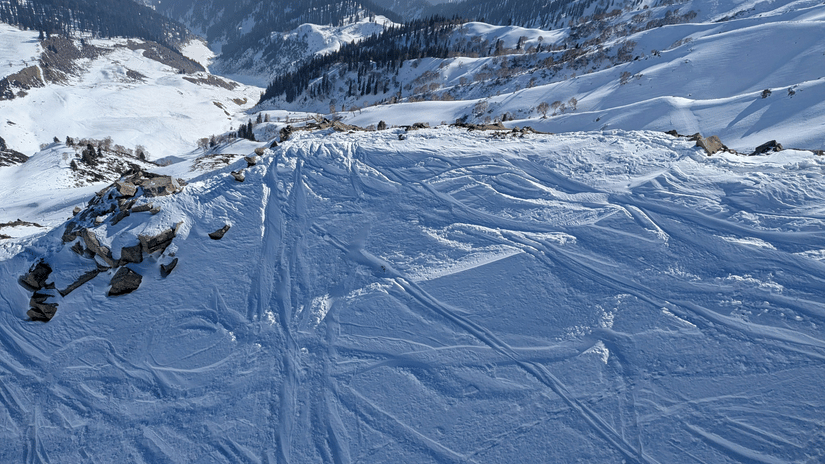 A steep, wide expanse of white snow with numerous ski tracks running through it, high in the mountains.