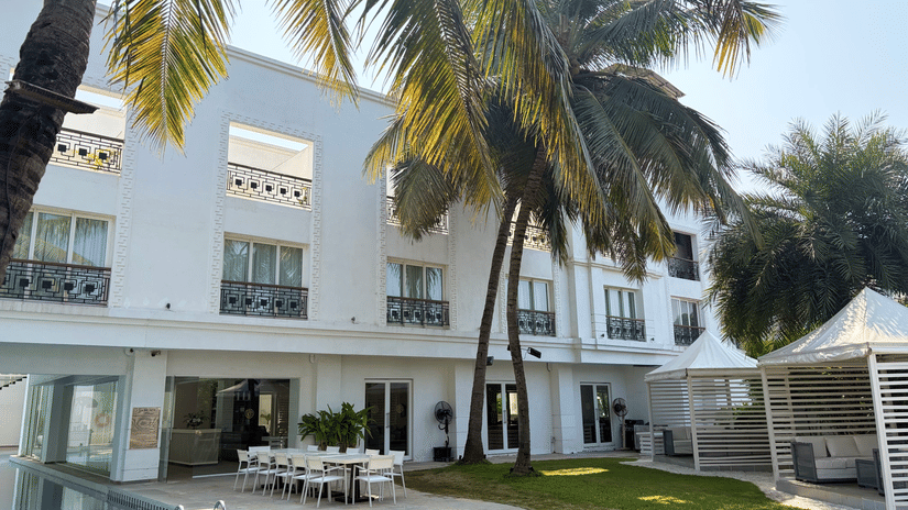 The Mansion House luxury resort exterior with white multi-story building, palm trees, swimming pool, outdoor dining setup, and gazebo, creating a tropical and serene vacation atmosphere.