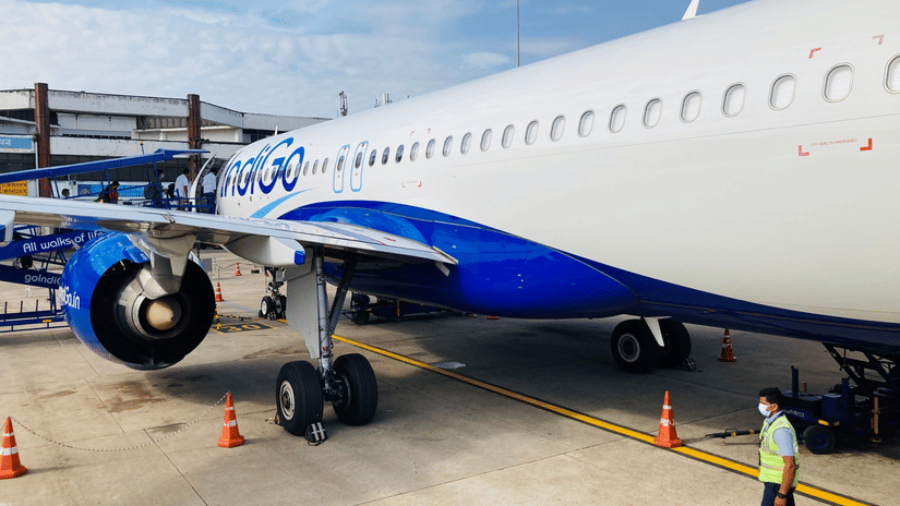 Commercial airplane parked on an airport tarmac, with a ground crew member nearby and a boarding staircase positioned beside the aircraft.