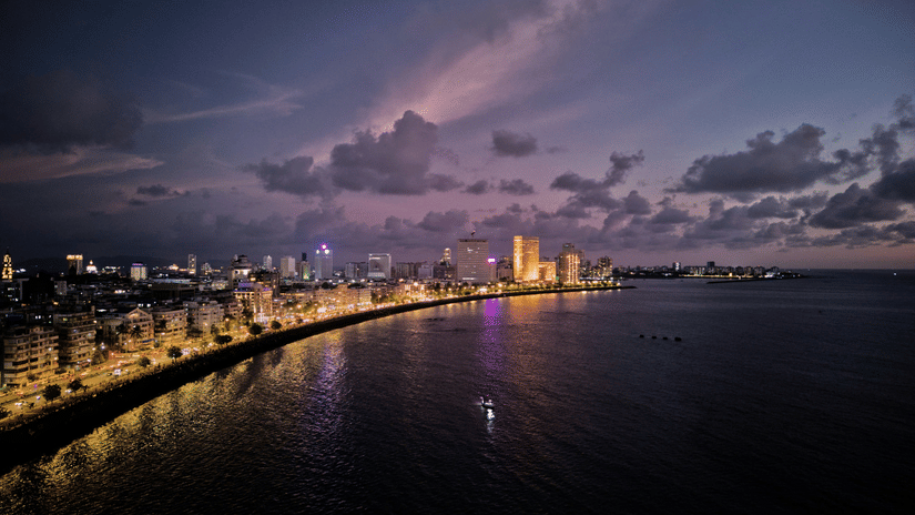 Evening view of a coastal city promenade with illuminated buildings and reflections across the waterfront