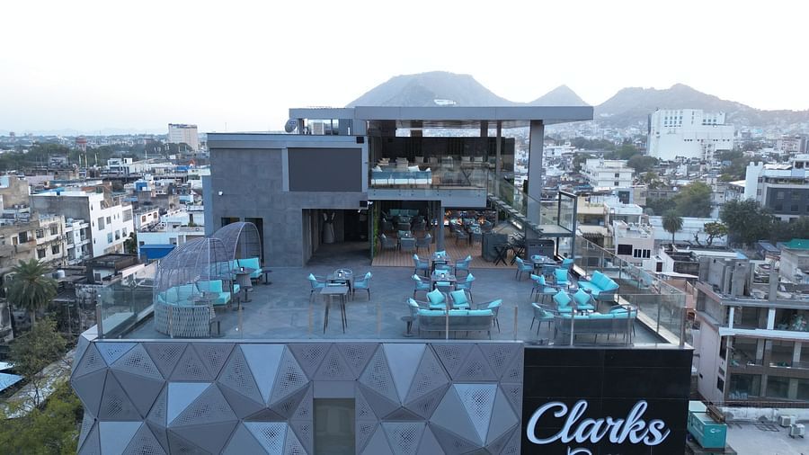 A long shot view of a rooftop restaurant with neatly arranged tables and chairs, offering a scenic backdrop of mountains at Clarks Collection Grand Sapphire, Ajmer.