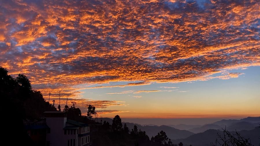 Fiery sunset clouds streak across the sky, their vibrant orange hues contrasting with the dark silhouettes of the mountain range, creating a dramatic and captivating scene, possibly seen from the resort