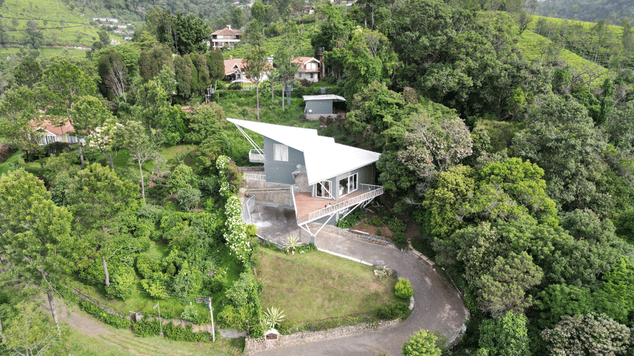 Elevated view of a house set against forested hills under a cloudy sky at Ibex Resorts, Coonoor (Tapas).