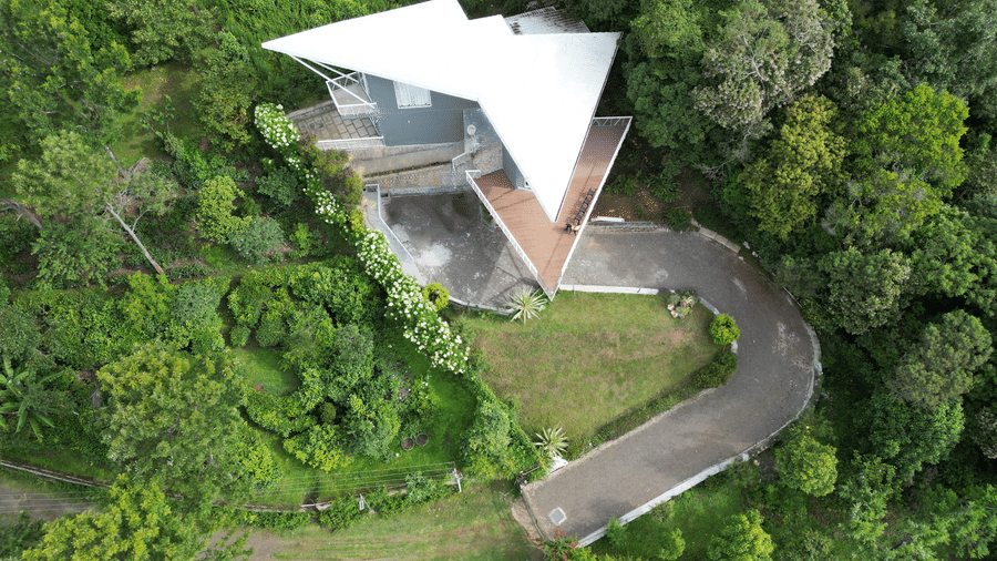 A light-colored modern villa surrounded by tall trees and tropical vegetation in daylight at Ibex Resorts, Coonoor (Tapas).