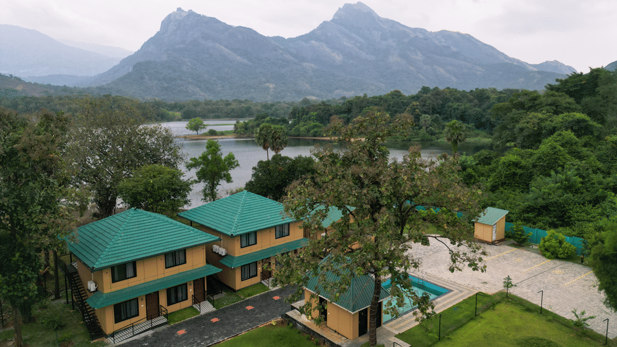 High-angle landscape view of the resort buildings situated between a calm lake and towering mountain peaks - Ibex Resorts, Malampuzha (Kava Eco Camp and Caravan Park)