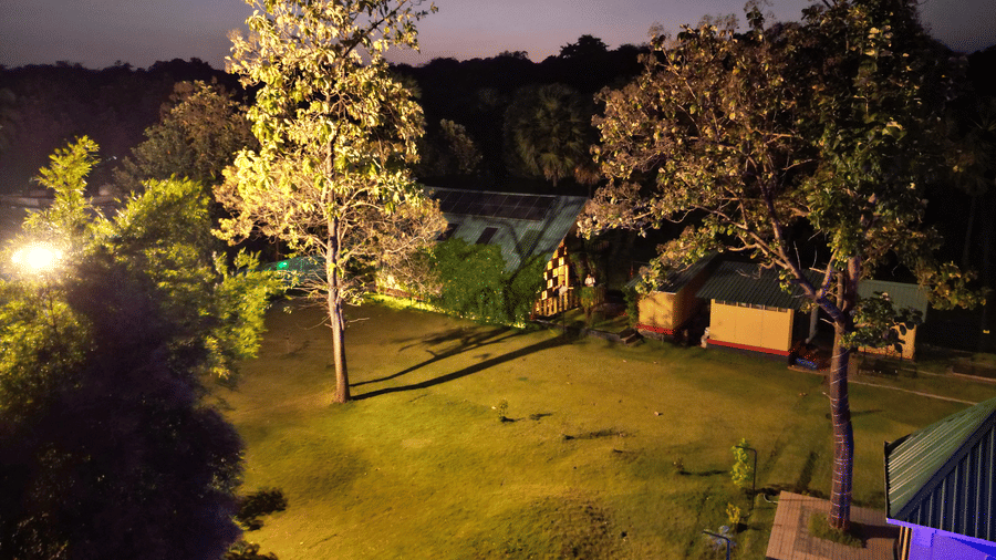 The illuminated facade of Ibex Resorts, Malampuzha (Kava Eco Camp and Caravan Park), featuring trees, and greenery at night.
