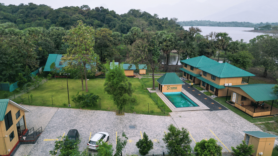 The illuminated facade of Ibex Resorts, Malampuzha (Kava Eco Camp and Caravan Park), featuring trees, greenery, and a pathway.