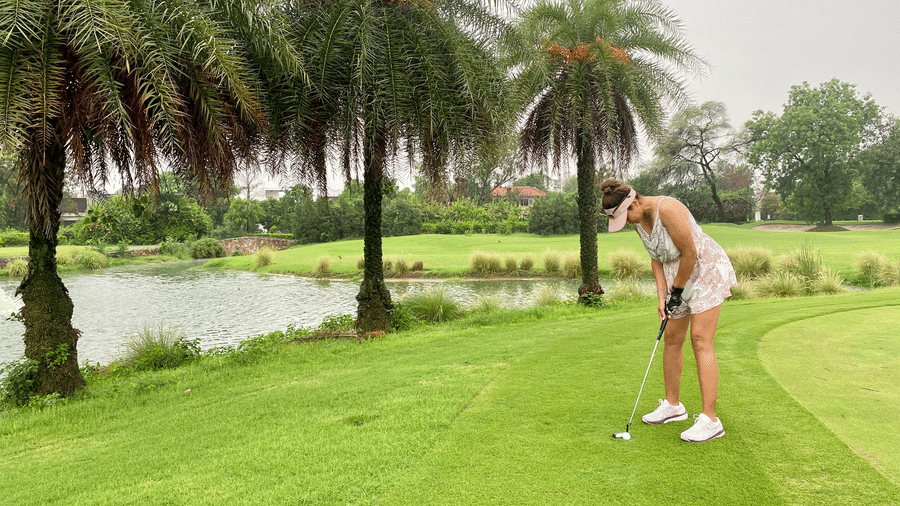 a woman playing golf at Karma Lakelands with trees and a sandpit in view.
