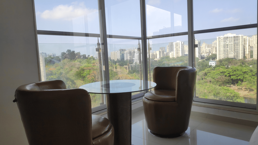 A shot of cup-shaped arm chairs and glass teapoy placed near a  huge glass window in a bedroom