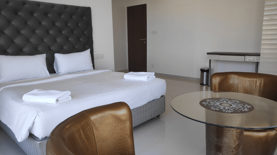 A full view of bedroom in a 2 BHK in Andheri East with a king size bed, 2 cup-shaped arm chairs and a glass teapoy