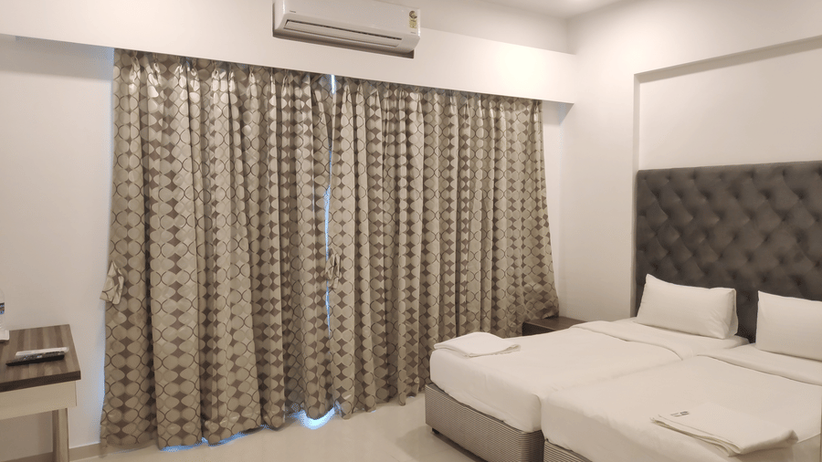 A view of a bedroom with an AC and twin beds in a 2 BHK service apartment in Andheri East