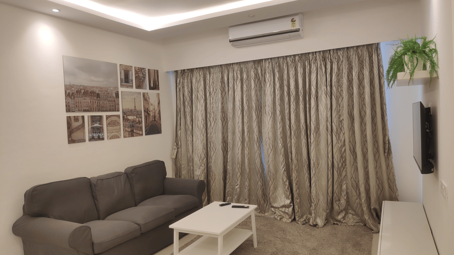 A picture of the living room with a grey couch and white coffee table on a beige rectangular rug and wallpapers on the wall in a 3 BHK service apartment in Andheri East