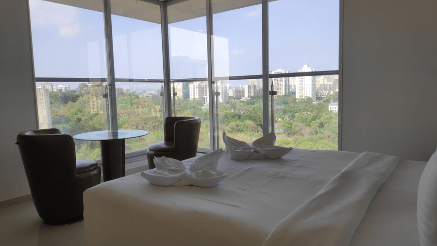 A view of a king size bed in a 3 BHK service apartment in Mumbai with cup-shaped arm chairs and a glass table