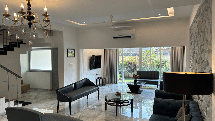 A grand living room with contemporary decor, a chandelier-lit ceiling, plush sofas, and a sleek black coffee table – Maxxvalue Klub Klass Villa, Lonavala.