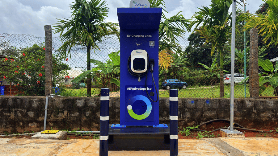 An electric vehicle (EV) charging point stands in an outdoor area surrounded by trees under a cloudy sky at MGM Whispering Wind's