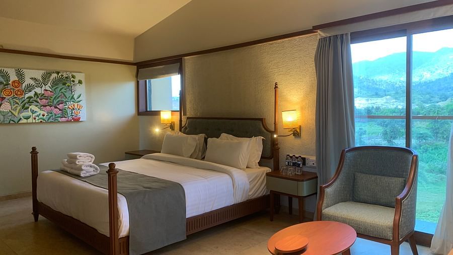 Side view of a double bed with grey bedsheet, an armchair and a small round table at Pride Resort Ambaji