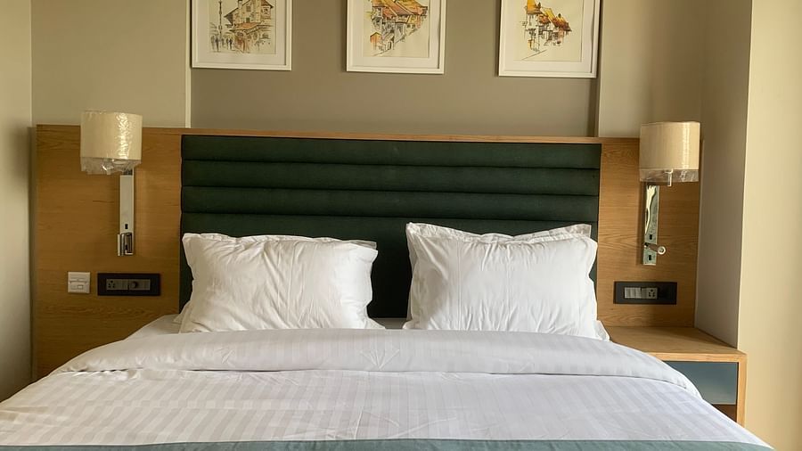 Front view of a double bed with grey besdsheet and two pillows and three white frames on the wall