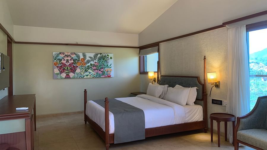 Side view of a double bed with grey bedsheet, an armchair and a small round table and a beautiful painting on the wall at Pride Resort near Ambaji Temple.