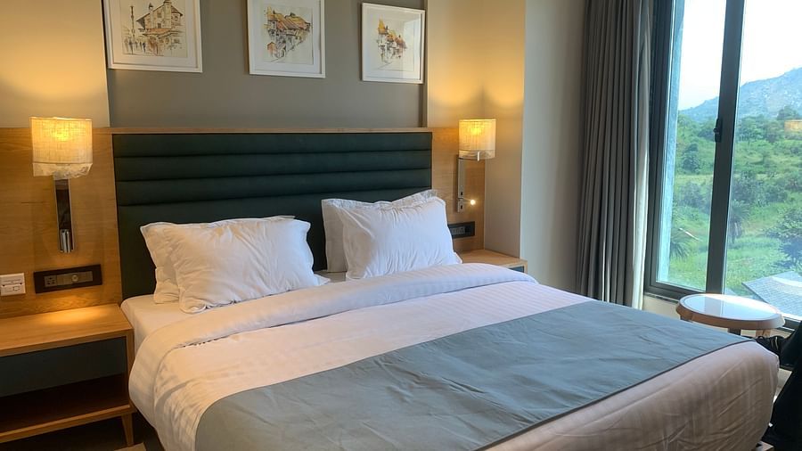 Image of a double bed with beautiful blue sheet and two white pillows with three frames hanging on the wall at Pride Resort near Ambaji Temple.