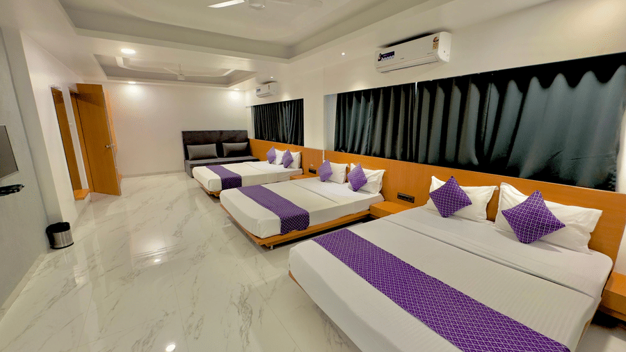 Wide view of the family room at Pushpak Resort, Shirdi, with multiple beds and modern interiors.