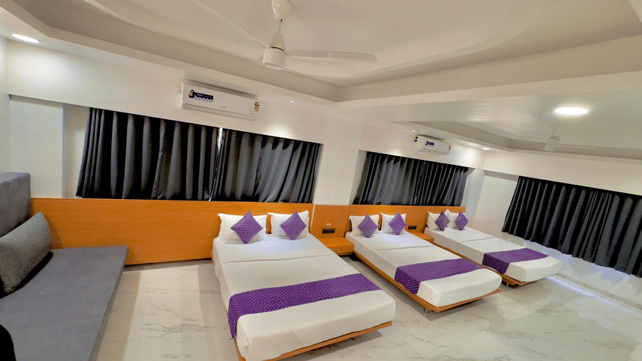 Large room at Pushpak Resort, Shirdi, furnished with three beds, curtains, and a sofa for group stays.