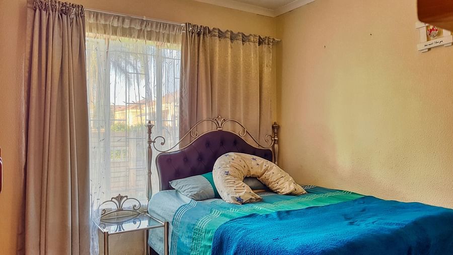 A bedroom featuring a double bed with blue sheets spread neatly over it with beige curtains covering the window behind it.
