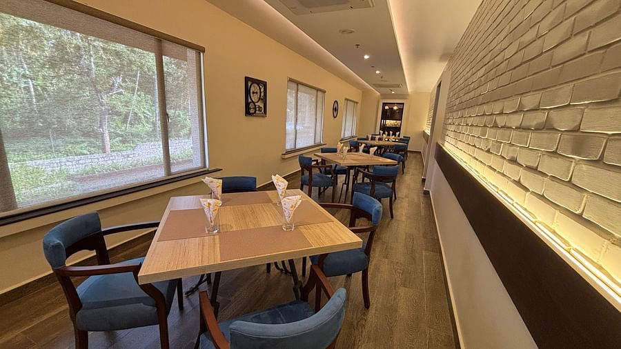 A brightly lit dining area at Chef's Table with wooden tables and blue chairs with an outdoor view through the glass. - Still Waters, Varkala