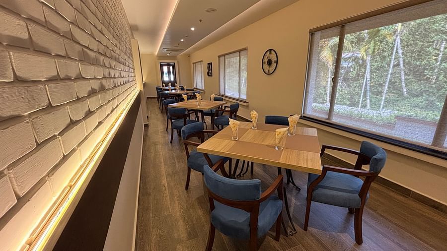 A brightly lit dining area with wooden tables and blue chairs, and a long display case along one wall. - Still Waters, Varkala