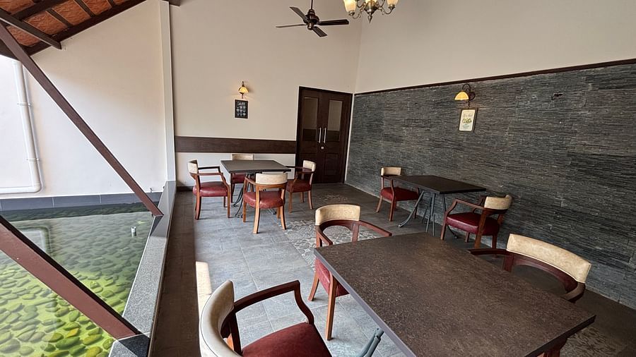 Dining area with several wooden tables and chairs, and a partial view of the roof with brown tiles. - Still Waters, Varkala