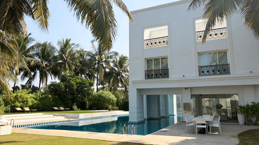 The Mansion House luxury resort exterior with modern two-story white building, balconies, swimming pool, palm trees, and outdoor seating, creating a serene tropical atmosphere