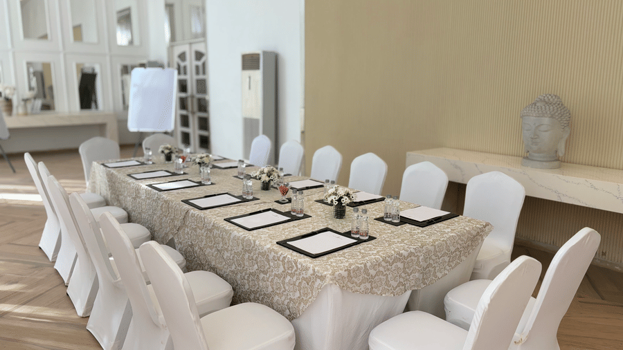 The Mansion House resort meeting setup with long rectangular table, beige tablecloth, white-covered chairs, notepads, and floral arrangements, designed for conferences or formal gatherings.