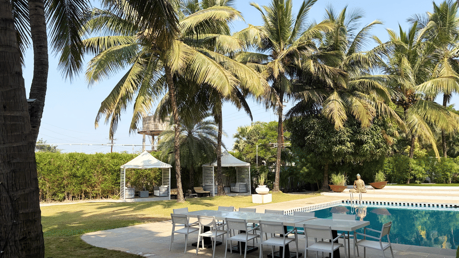 The Mansion House resort poolside dining with long white table, chairs, canopy tents, palm trees, and tall structure, offering a tropical and inviting atmosphere for gatherings.