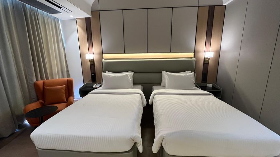 A Deluxe room features two single beds with white linens, upholstered headboards, bedside tables, and a glimpse of a seating area - The Orchid Hotel, Chandigarh