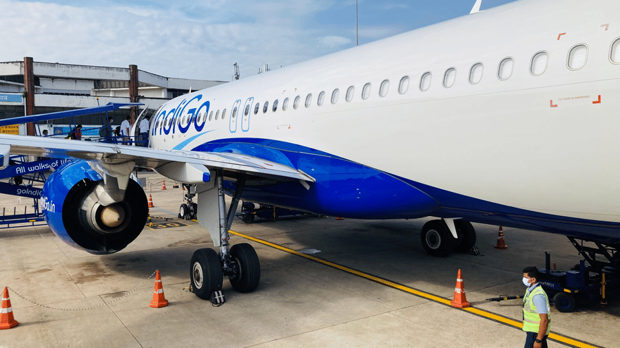 Commercial airplane parked on an airport tarmac, with a ground crew member nearby and a boarding staircase positioned beside the aircraft.