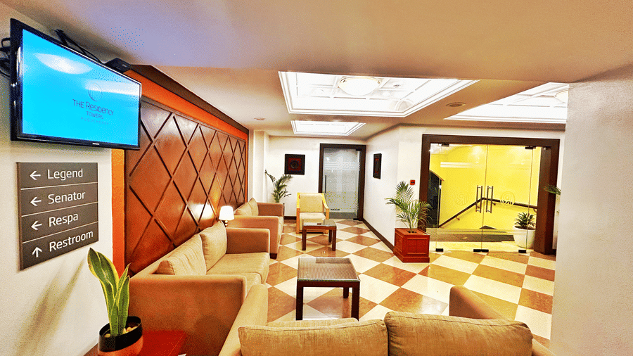 A seating area with sofas, television, a plant, and doors. | The Residency Karur