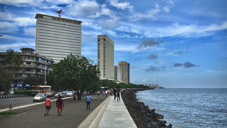 An overview of the Marine Drive with people walking on the sidewalk next to the Arabian Sea. Marine Drive is one of the must-visit place on your things to do in Mumbai during monsoons.