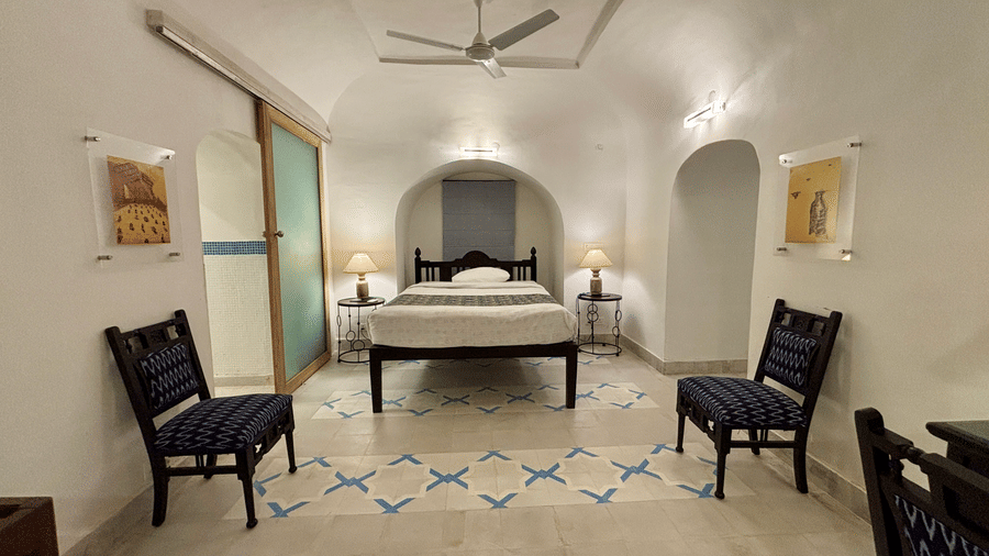 Spacious room view at Tijara Fort-Palace - 19th Century, Alwar, showing a central bed, ceiling fan, and patterned tile flooring.
