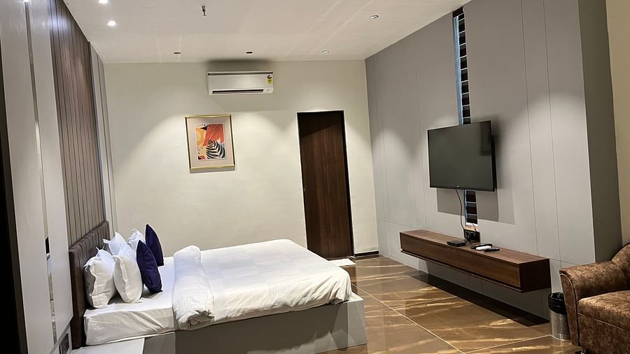 A king bed with an ac and tv wall mounted inside super deluxe room - VITS Jamnagar, Mithoi