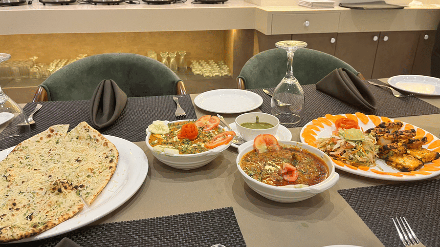 A close up of the table at Aromas restaurant featuring Indian bread, charred paneer starter, and two bowls of curry | VITS Jamnagar, Mithoi