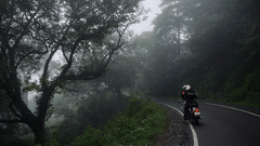 A person on a motorcycle rides along a winding road through a foggy, forested area | Himavad Gopalaswamy Temple history
