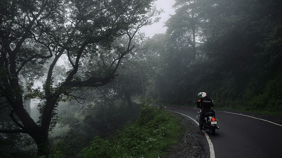 A person on a motorcycle rides along a winding road through a foggy, forested area | Himavad Gopalaswamy Temple history