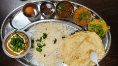 A view of an Indian thali served in a steel plate with many sides, rice, curry and papad.