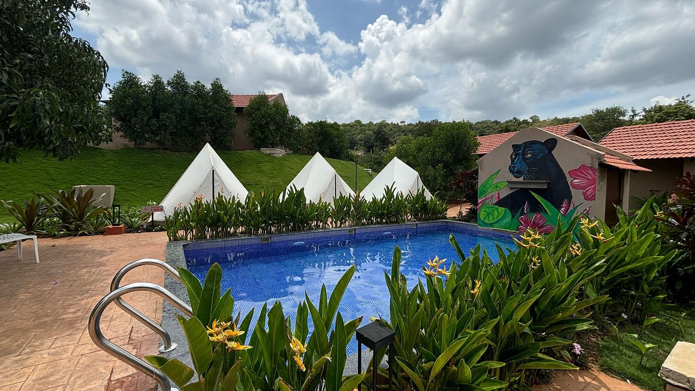 A scenic view of a resort area with pool and tents lined along a neat walkway, surrounded by a well-maintained lawn.