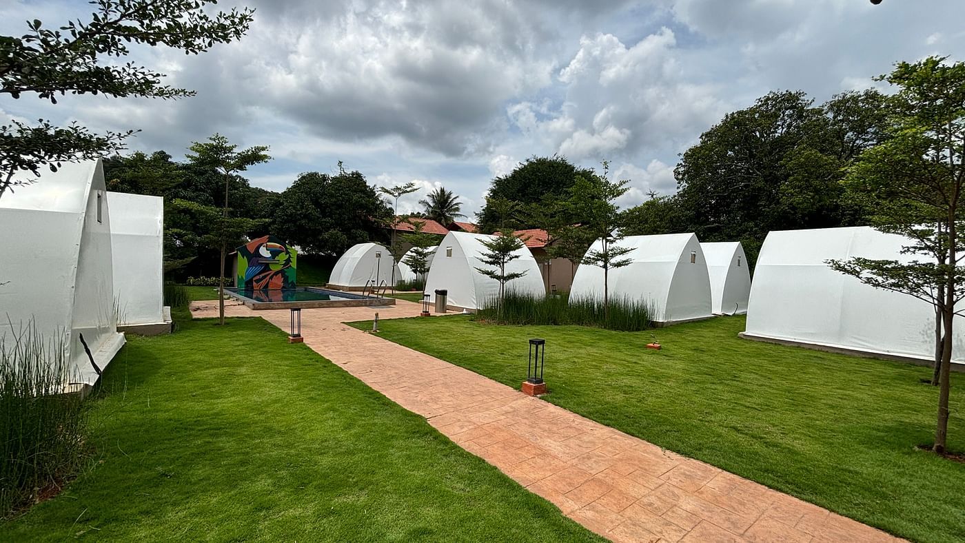  A scenic view of a resort area with tents lined along a neat walkway, surrounded by a well-maintained lawn.