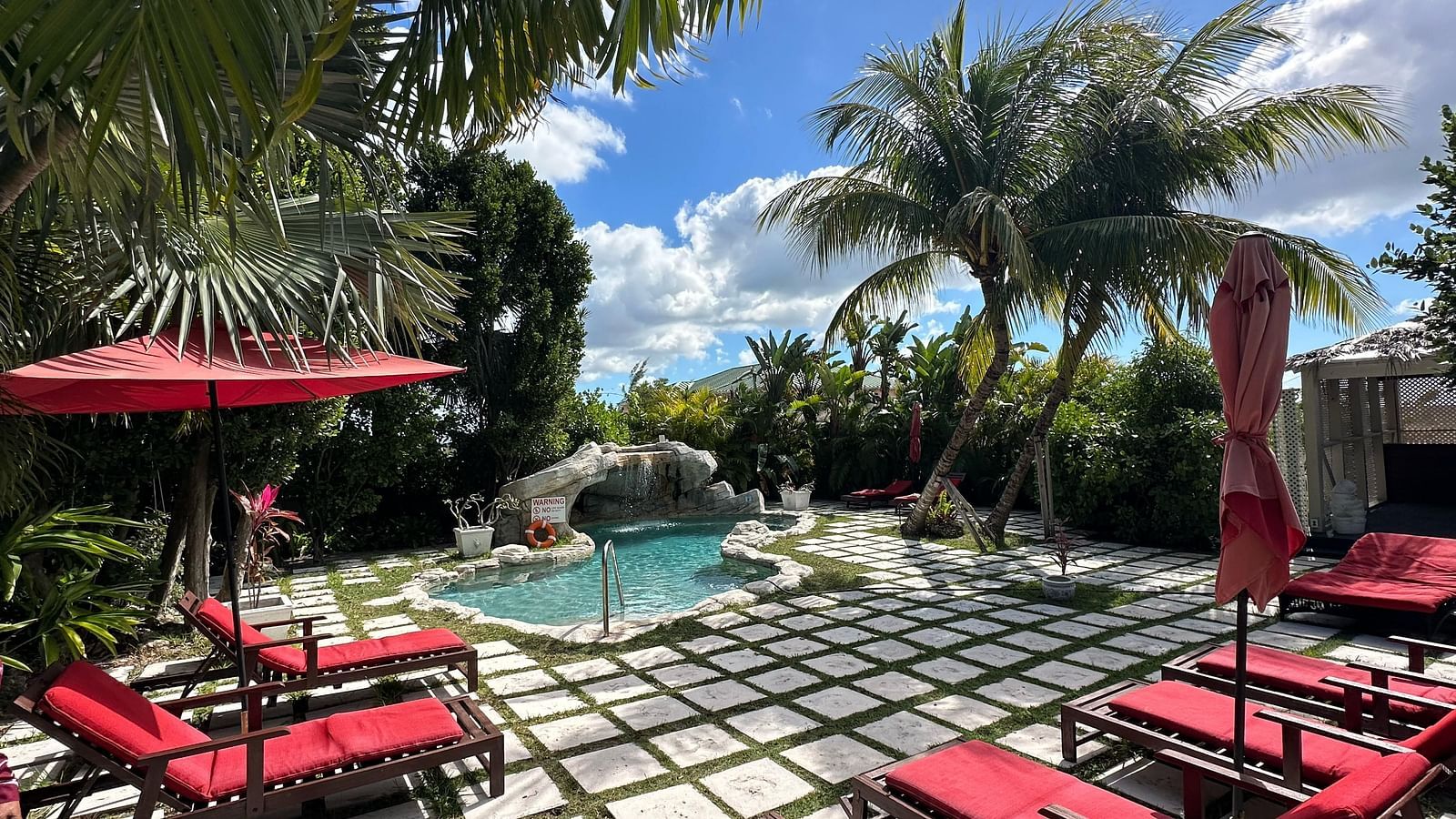 Poolside seating with red lounge chairs and umbrellas surrounded by palm trees | A Stone's Throw Away
