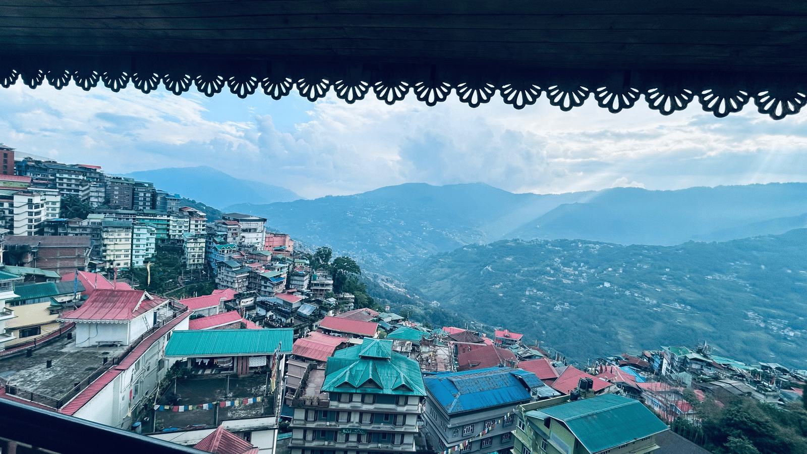 Colorful hillside houses and buildings in Gangtok city with mountains in the background under a cloudy sky.