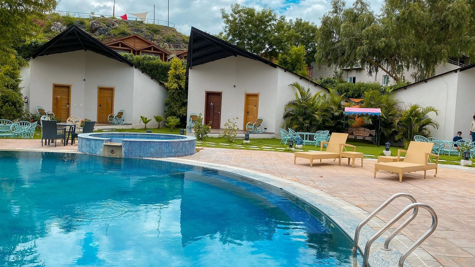 Two buildings beside a pool, with hills in the background.